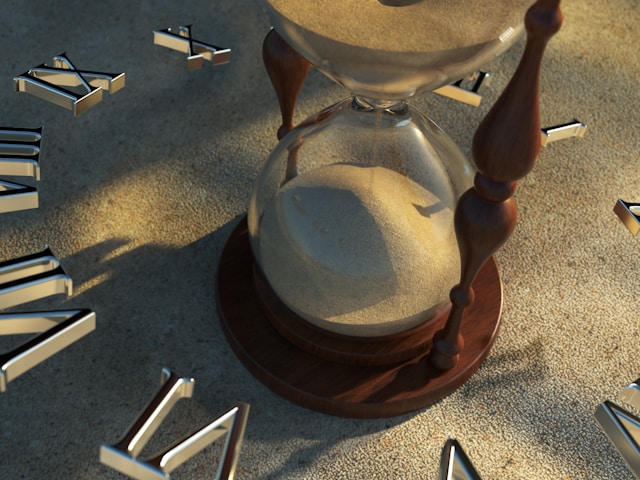 Hourglass with sand running through, surrounded by scattered Roman numerals, representing time and a late financial start for physicians.