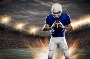 A young football player holding a ball on a floodlit field, illustrating an article on NIL financial planning for athletes and their families.