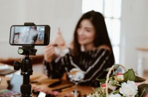 A content creator filming a makeup tutorial on a smartphone mounted on a tripod, representing financial planning for social media influencers.